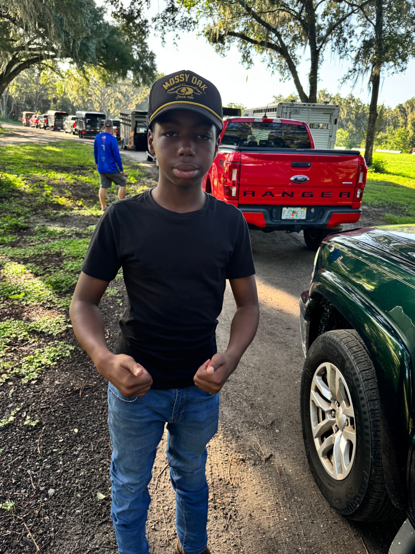 Ethan wearing his Mossy Oak hat at a livestock event beneath oak trees